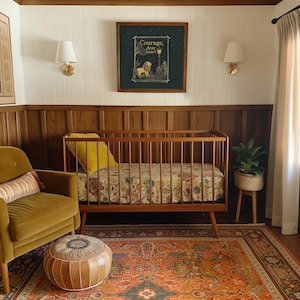 May include: A mid-century modern nursery with a wooden crib, a mustard-colored armchair, and a patterned rug. A framed print with the text "Courage, dear heart" hangs above the crib. A small plant in a woven pot sits on a wooden stand.