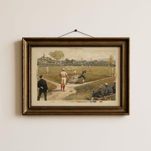 May include: A framed vintage baseball print. The artwork depicts a baseball game in progress, with players in period uniforms on a green field. The frame is a dark, ornate wood. The print has a sepia tone.