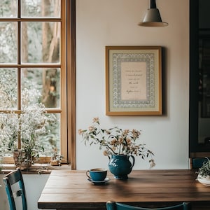 May include: A framed wall art print featuring the text When my heart is overwhelmed lead me to the rock that is higher than I Psalm 61:2, displayed in a light wood frame with a decorative border, hanging on a white wall above a wooden table.