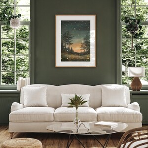 Puede incluir: Un sof&aacute; blanco con dos almohadas se encuentra en una sala de estar con una pared verde. Un cuadro enmarcado de una escena de bosque con un cielo estrellado cuelga sobre el sof&aacute;. Una mesa de caf&eacute; de vidrio se encuentra frente al sof&aacute; con un libro encima. Una cesta tejida se encuentra en el suelo junto al sof&aacute;.