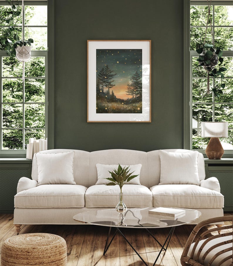 Puede incluir: Un sof&aacute; blanco con dos almohadas se encuentra en una sala de estar con una pared verde. Un cuadro enmarcado de una escena de bosque con un cielo estrellado cuelga sobre el sof&aacute;. Una mesa de caf&eacute; de vidrio se encuentra frente al sof&aacute; con un libro encima. Una cesta tejida se encuentra en el suelo junto al sof&aacute;.