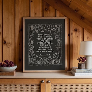 May include: A framed print with a black background and white floral border. The text reads: "YOUR CUSTOM QUOTE, POEM, VERSE OR LYRICS LIVE HERE. PERFECT FOR A GIFT OR A MEMORABLE KEEPSAKE FOR YOUR OWN SPACE."