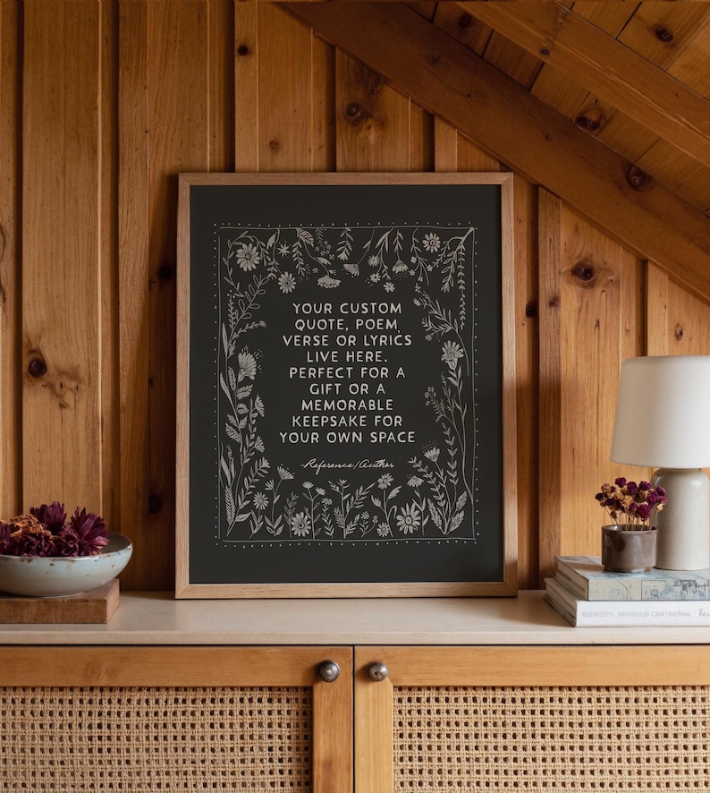 May include: A framed print with a black background and white floral border. The text reads: "YOUR CUSTOM QUOTE, POEM, VERSE OR LYRICS LIVE HERE. PERFECT FOR A GIFT OR A MEMORABLE KEEPSAKE FOR YOUR OWN SPACE."