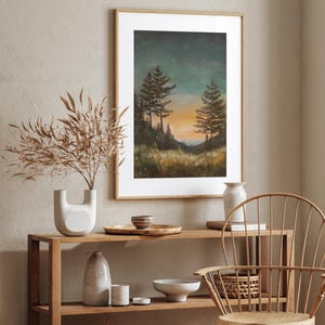 May include: A framed print of a painting depicting a forest scene at dusk. The painting features three tall trees silhouetted against a sky filled with stars. The sky is a deep blue with hints of orange and purple. The trees are dark green and brown. The ground is covered in grass and bushes. The painting is set in a wooden frame.