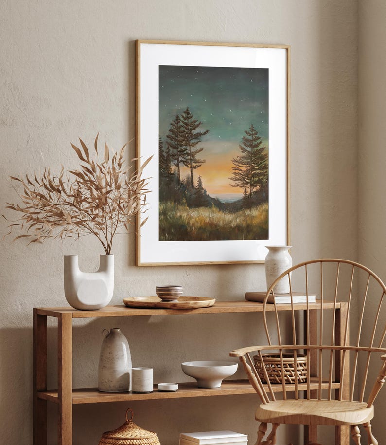 May include: A framed print of a painting depicting a forest scene at dusk. The painting features three tall trees silhouetted against a sky filled with stars. The sky is a deep blue with hints of orange and purple. The trees are dark green and brown. The ground is covered in grass and bushes. The painting is set in a wooden frame.