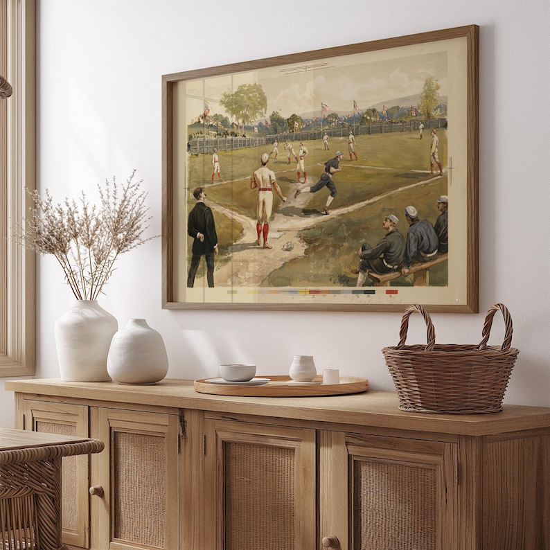 May include: A framed vintage baseball print depicting a game in progress. The artwork features players in period uniforms on a green field, with spectators and a wooden frame. The color palette includes greens, browns, and whites.