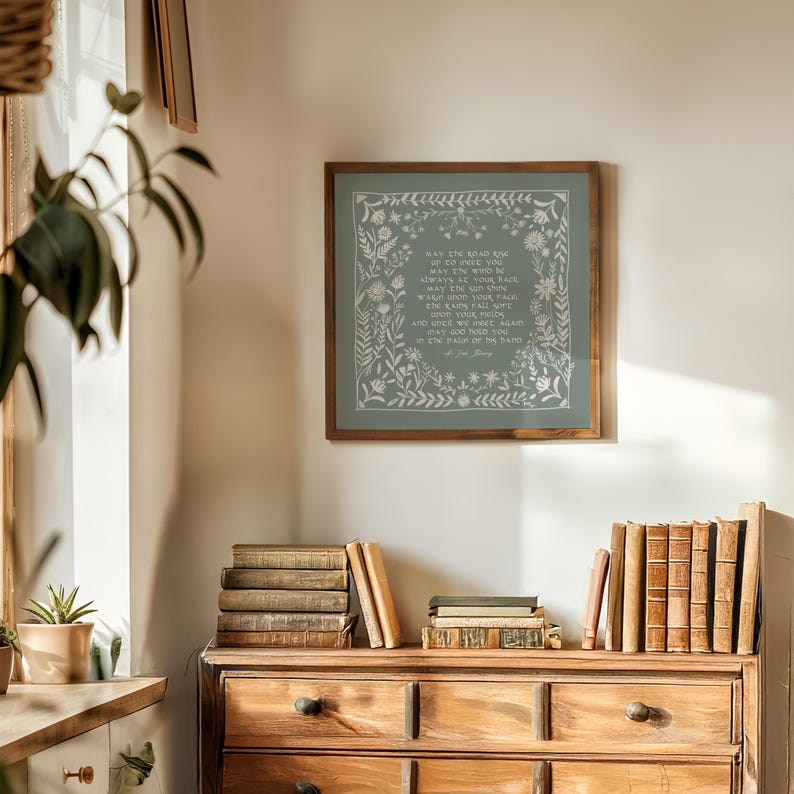 Peut inclure: Une impression encadr&eacute;e avec un fond bleu clair et une bordure florale blanche. L'impression pr&eacute;sente un po&egrave;me avec le texte "Que la route s'&eacute;l&egrave;ve pour vous rencontrer. Que le vent soit toujours dans votre dos. Que le soleil brille chaud sur votre visage. Que la pluie tombe doucement sur vos champs et jusqu'&agrave; ce que nous nous rencontrions &agrave; nouveau, que Dieu vous tienne dans la paume de sa main."