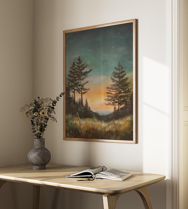 May include: A framed painting of a forest scene at sunset with two pine trees in the foreground and a starry sky above. The painting is in a wooden frame and is hanging on a wall.