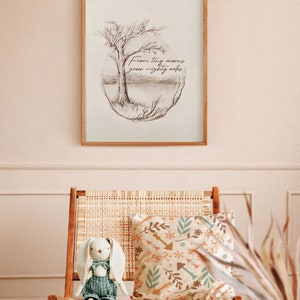 Puede incluir: Una impresi&oacute;n enmarcada con un dibujo a l&aacute;piz de un &aacute;rbol y el texto "From tiny acorns grow mighty oaks". La impresi&oacute;n est&aacute; colgada en una pared rosa claro sobre una silla de mimbre con un coj&iacute;n estampado y un conejito de peluche.