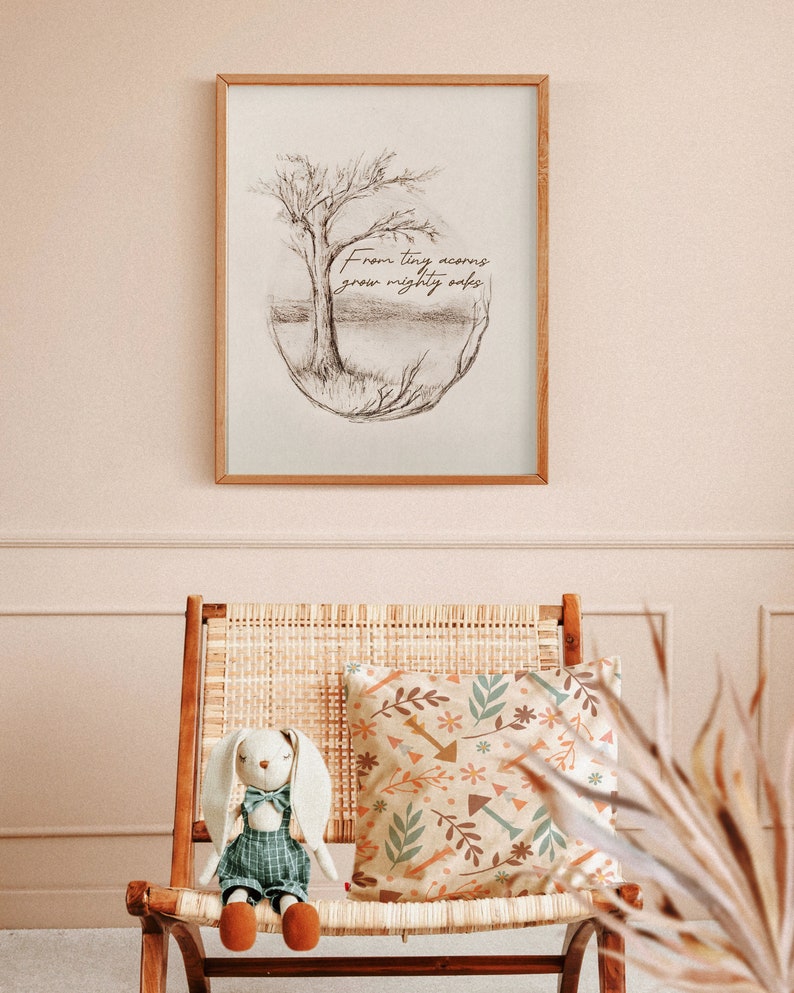 Puede incluir: Una impresi&oacute;n enmarcada con un dibujo a l&aacute;piz de un &aacute;rbol y el texto "From tiny acorns grow mighty oaks". La impresi&oacute;n est&aacute; colgada en una pared rosa claro sobre una silla de mimbre con un coj&iacute;n estampado y un conejito de peluche.