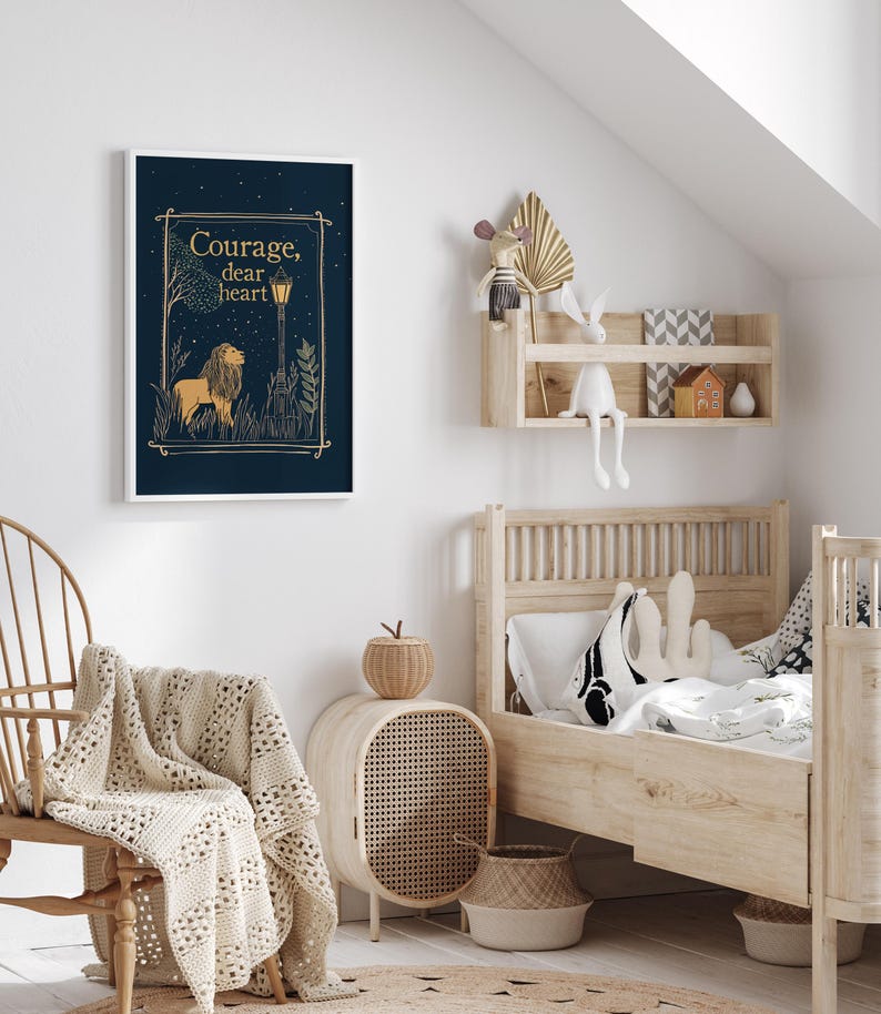 May include: A framed art print with a navy blue background features a lion illustration and the words "Courage, dear heart" in gold. The artwork is displayed in a child's bedroom with a wooden bed and decorative shelf.