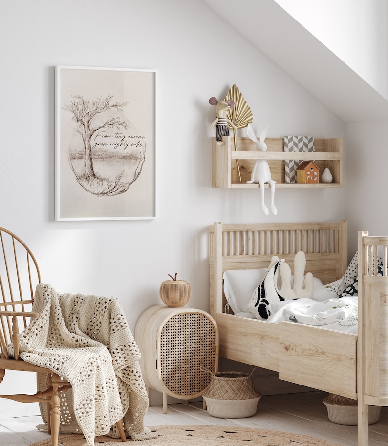 Puede incluir: Una impresi&oacute;n enmarcada en blanco con un dibujo a l&aacute;piz de un &aacute;rbol y el texto "From tiny acorns grow mighty oaks". La impresi&oacute;n est&aacute; colgada en una pared blanca en una guarder&iacute;a con una cama de madera, una silla de mimbre y un peque&ntilde;o estante de madera con una figurita de conejo.