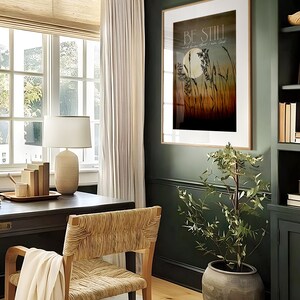 May include: A framed print with the text "Be Still and know that I am God" in a modern home office setting. The print features a moon and tall grass in a sunset color palette.