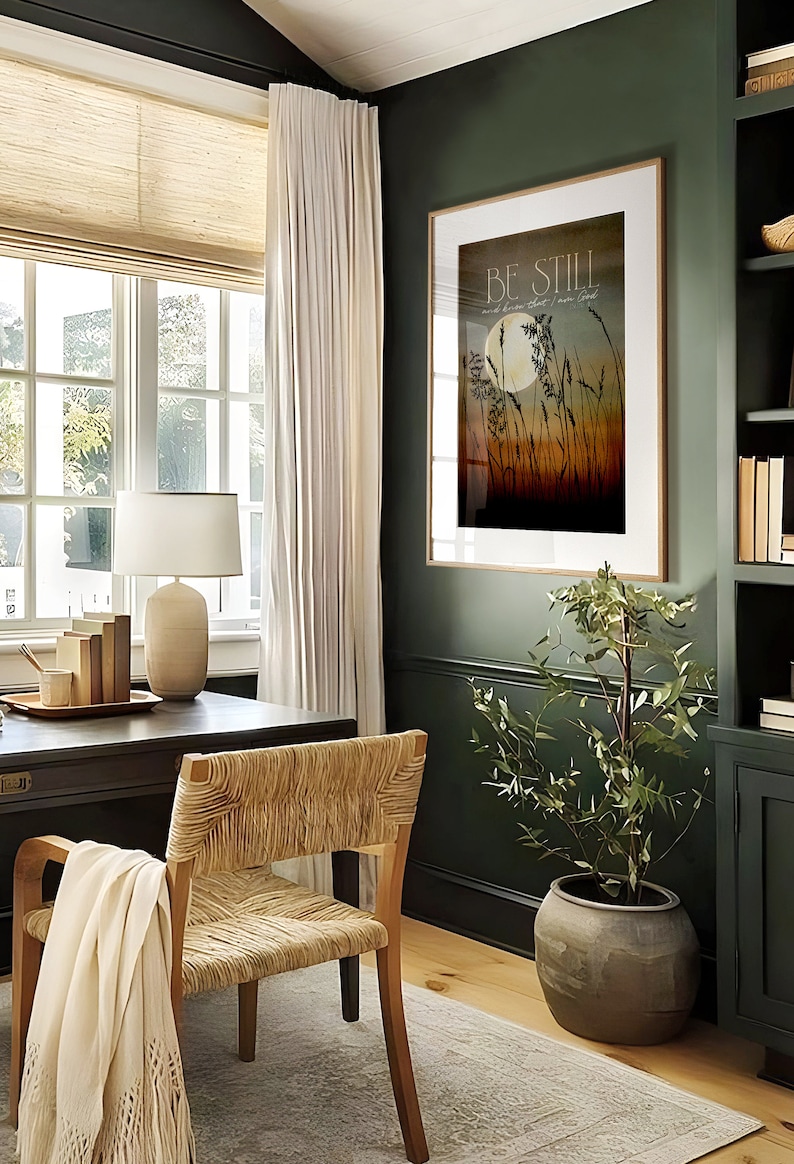 May include: A framed print with the text "Be Still and know that I am God" in a modern home office setting. The print features a moon and tall grass in a sunset color palette.