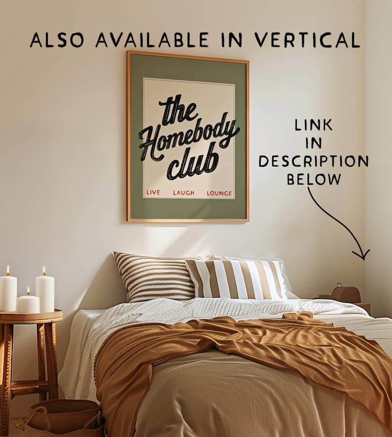 May include: A framed poster with the text "the Homebody club" in black script, above the words "LIVE LAUGH LOUNGE" in a red font. The poster hangs above a bed with pillows and a brown blanket. Candles sit on a wooden side table.