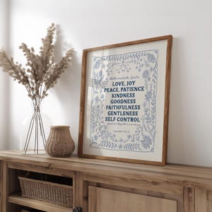 May include: A framed print with a white background and blue floral border. The text inside the frame reads "But the fruit of the Spirit is Love, Joy, Peace, Patience, Kindness, Goodness, Faithfulness, Gentleness, Self Control. Galatians 5:22-23".
