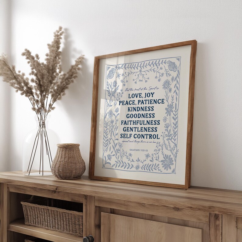 May include: A framed print with a white background and blue floral border. The text inside the frame reads "But the fruit of the Spirit is Love, Joy, Peace, Patience, Kindness, Goodness, Faithfulness, Gentleness, Self Control. Galatians 5:22-23".