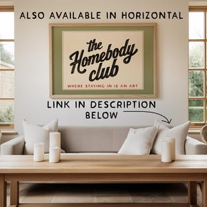 K&ouml;nnte beinhalten: Ein gerahmtes Poster mit dem Text "the Homebody club" in schwarzer Schrift, mit den Worten "WHERE STAYING IN IS AN ART" darunter. Das Poster befindet sich &uuml;ber einem hellen Sofa mit wei&szlig;en Kissen und einem Holztisch.