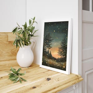 Puede incluir: Una impresi&oacute;n enmarcada de una pintura que representa una escena de bosque al atardecer. El cielo es azul oscuro con algunas estrellas y una puesta de sol naranja brillante. Dos &aacute;rboles se alzan en primer plano, con un campo de hierba y luces brillantes en la distancia.