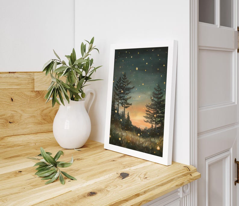 Puede incluir: Una impresi&oacute;n enmarcada de una pintura que representa una escena de bosque al atardecer. El cielo es azul oscuro con algunas estrellas y una puesta de sol naranja brillante. Dos &aacute;rboles se alzan en primer plano, con un campo de hierba y luces brillantes en la distancia.