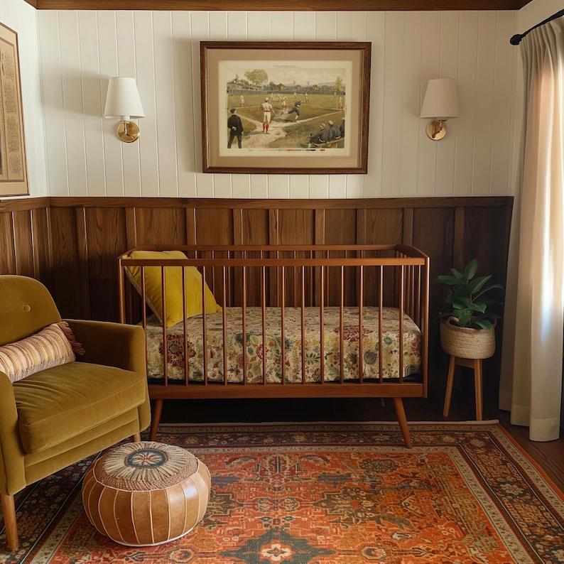 May include: A cozy nursery with a wooden crib, a patterned rug, and a mustard-colored armchair. The crib has a floral patterned mattress and a yellow pillow. A framed vintage baseball print hangs above the crib, and a small plant sits on a side table.