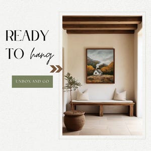 May include: A framed landscape painting of a small white house with a chimney in a forest setting. The painting is hanging on a white wall in a room with wooden beams and a wooden bench. The painting is ready to hang.