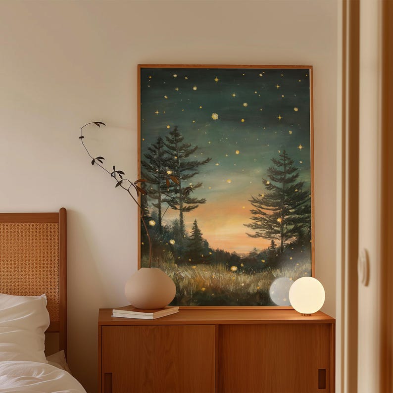 Puede incluir: Una pintura enmarcada de una escena de bosque nocturno con un cielo estrellado. La pintura est&aacute; sobre una c&oacute;moda de madera con una l&aacute;mpara y un jarr&oacute;n con una planta.
