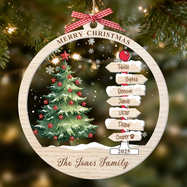 Puede incluir: Un adorno navideño redondo de madera con un árbol verde y estrellas rojas, una señal con los nombres Tobias, Sophia, Benson, Jamie, Victor, Drew y Cooper, los textos Merry Christmas, 2025 y The Jones Family, rematado con un lazo de cuadros rojo.