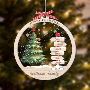 May include: A round wooden Christmas ornament featuring a green tree with red stars, a signpost with names Donald, Astrid, Victoria, Teman, Jacob, and Luna, the text Merry Christmas, 2025, and Williams Family, topped with a red and white gingham bow.