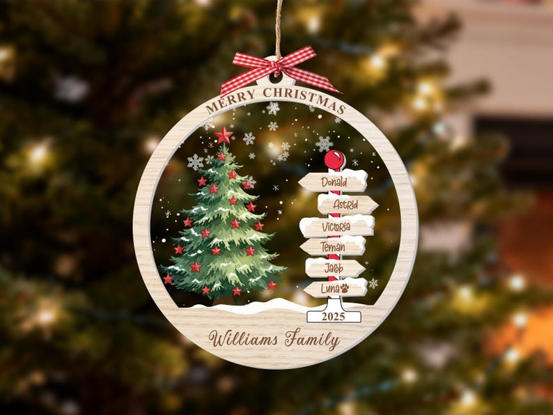 May include: A round wooden Christmas ornament featuring a green tree with red stars, a signpost with names Donald, Astrid, Victoria, Teman, Jacob, and Luna, the text Merry Christmas, 2025, and Williams Family, topped with a red and white gingham bow.