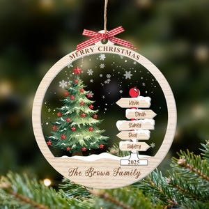 May include: A round wooden Christmas ornament featuring a green tree with red stars, a signpost with the names Kevin, Dinah, Sidney, Rose, and Hubery, the text Merry Christmas, 2025, and The Brown Family, topped with a red and white gingham bow.