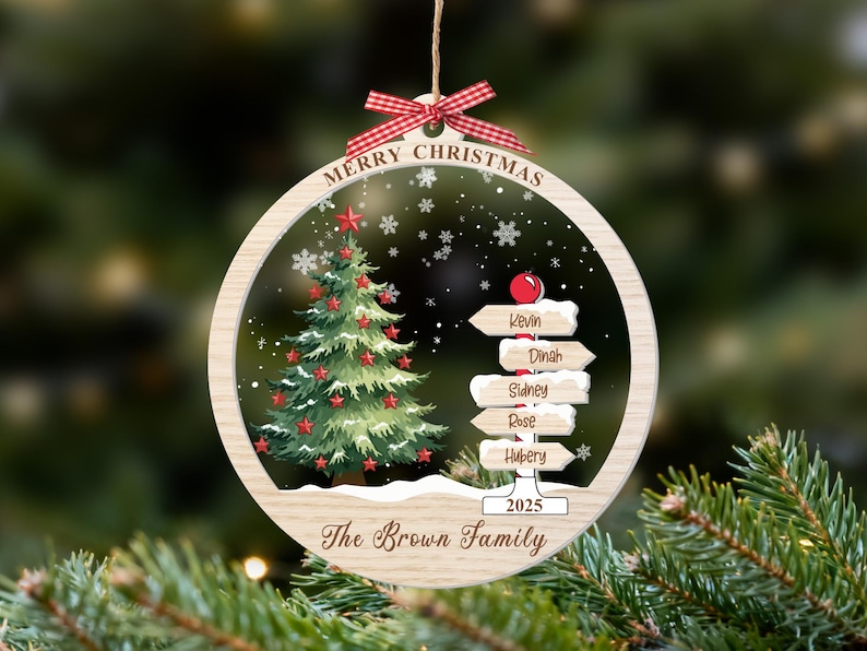 May include: A round wooden Christmas ornament featuring a green tree with red stars, a signpost with the names Kevin, Dinah, Sidney, Rose, and Hubery, the text Merry Christmas, 2025, and The Brown Family, topped with a red and white gingham bow.