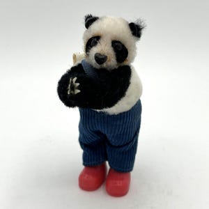 May include: A panda bear ornament with black and white fur, dressed in blue corduroy trousers and red boots. The panda has black eyes and ears, and is holding a small object.