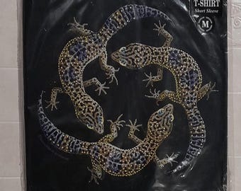 Może przedstawiać: Czarny T-shirt z grafiką przedstawiającą trzy gekony w kółku. Gekony są czarne, brązowe i złote z białymi plamkami. Koszulka jest o kroju pełnym, z krótkim rękawem i w rozmiarze M.