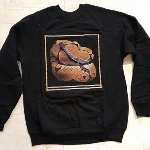 May include: Black sweatshirt featuring a graphic of a brown and yellow snake on the front.