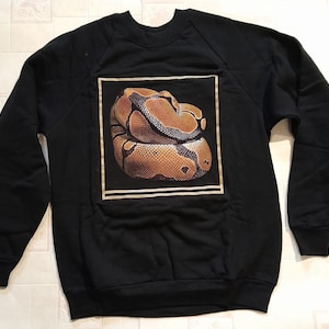 May include: Black sweatshirt featuring a graphic of a brown and yellow snake on the front.