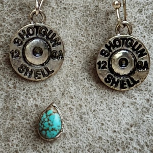 Könnte beinhalten: Silberfarbene Ohrringe mit einem Schrotpatronen-Design, mit dem Text "SHOTGUN SHELL 12 GA." Ein tropfenförmiger Türkisstein ist ebenfalls vorhanden. Die Ohrringe haben eine rustikale, Vintage-Ästhetik.