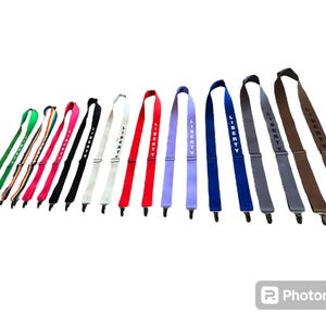 May include: A collection of suspenders in various colors, including green, pink, black, white, red, purple, blue, gray, and brown. Each suspender features the word "LIBERTY" printed in white or black and has metal clips.