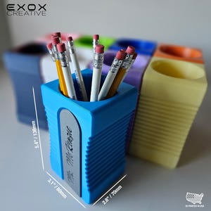 May include: A blue pencil holder shaped like a pencil sharpener, with dimensions of 5.4 inches high, 3.1 inches wide, and 2.8 inches deep. The holder contains several pencils. The text "Mc Renzie" is visible on the side. Other colored holders are in the background.