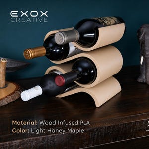 May include: A light honey maple colored wine rack made of wood infused PLA, featuring a curved, wave-like design that holds three wine bottles horizontally. The rack displays the text EXOX CREATIVE, Material: Wood Infused PLA, and Color: Light Honey Maple.