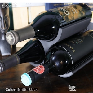 May include: Matte black wine rack holding three bottles of wine. The rack is designed to cradle the bottles at an angle. The bottles are dark with labels visible. The rack is made in the USA.