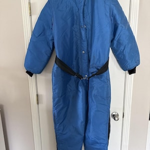 May include: A vintage blue snowsuit with a black belt and collar. The one-piece suit has a quilted design, long sleeves, and black cuffs. The suit has the brand name "IGLOO by Champion" on the collar.