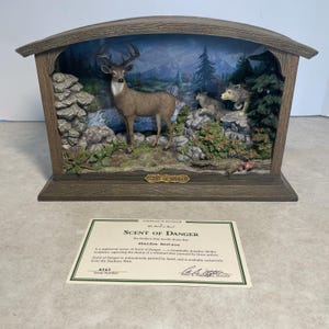 May include: A detailed diorama titled "Scent of Danger" featuring a deer and wolves in a forest setting. The sculpture is housed in a wooden frame with a scenic backdrop. The diorama includes the text "Scent of Danger" on the base.
