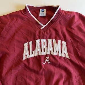May include: A maroon pullover windbreaker with a white collar and trim. The word "ALABAMA" is embroidered in white across the chest, with a white "A" below. The NCAA logo is visible on the collar.