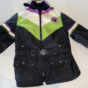 May include: Black and color-blocked winter jacket with a zip-up front, a belt, and two front pockets. The jacket features a color block design with green, white, and purple accents. The jacket has a hood and a circular emblem on the chest.