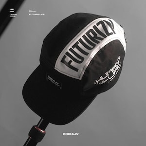 May include: Black and white baseball cap with the words "FUTURIZM" and "HUMAN LIFE" printed on it. The cap has a black brim and a white band around the top.