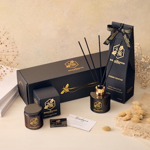 Op de afbeelding: Een cadeauset met geurproducten voor thuis in zwarte dozen met gouden accenten. De set bevat een kaars, een diffuser en een rietdiffuser. De producten zijn allemaal gelabeld met de merknaam "The Beekeeper Collection".