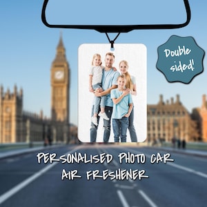 May include: A white photo car air freshener featuring a family of four in a photograph. The photo shows a man holding a young girl in his arms, a young girl standing next to him, and a young boy standing in front of him. The text "Double sided!" is in a blue circle on the right side of the image. The text "Personalised Photo Car Air Freshener" is below the image.