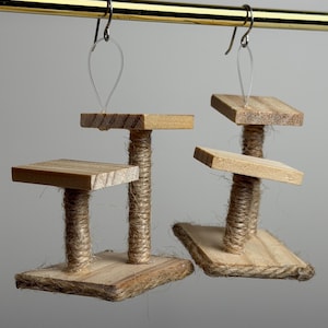May include: A pair of handmade wooden cat tree earrings. Each earring features a small, square base and platform, connected by a jute-wrapped post. The earrings hang from silver-colored fish hook ear wires. The wood has a natural, light brown color.