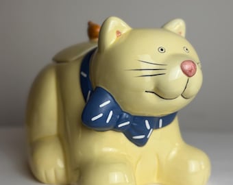 Tarro para galletas vintage con forma de gato amarillo: un caprichoso gato de cerámica con un lazo azul.